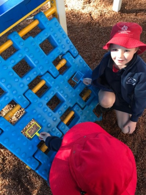 Prep students examine square shapes within playground climbing equipment, using shape frames to identify geometry in real-world environments.