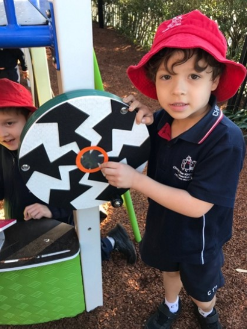 Prep student matches a circular shape frame to playground equipment, exploring 2D shapes through hands-on mathematical learning outdoors.
