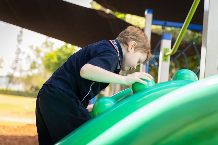 A boy in a navy blue t-shirt and shorts climbing on green play equipment.